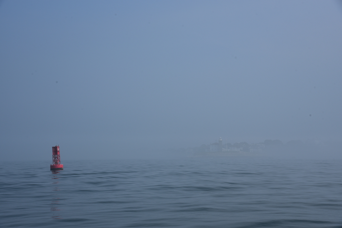 Boya roja en el paso de Watch Hill, con el faro en la niebla